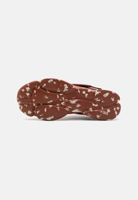 Suola di scarpa in gomma marrone con macchie bianche, caratterizzata da un design scolpito e scanalature per la trazione, che mostrano segni di usura lungo i bordi.