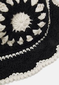 Chapeau seau en crochet noir et blanc présentant un motif circulaire, une surface texturée et un large bord noir uni avec un accent blanc.