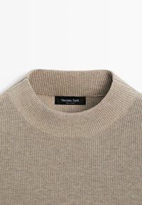Beiger gerippter Pullover mit weitem, strukturiertem Rundhalsausschnitt. Mit einem Etikett mit "Massimo Dutti" auf schwarzem Hintergrund. Weiches Strickmaterial.