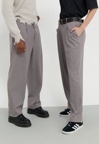 Light gray, wide-leg trousers with front pleats, worn with a black belt. One pair paired with black shoes, the other with black and white sneakers.