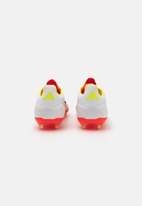 White soccer cleats with red accents, yellow highlights on the collar, and a textured surface. Features a molded heel and transparent sole.