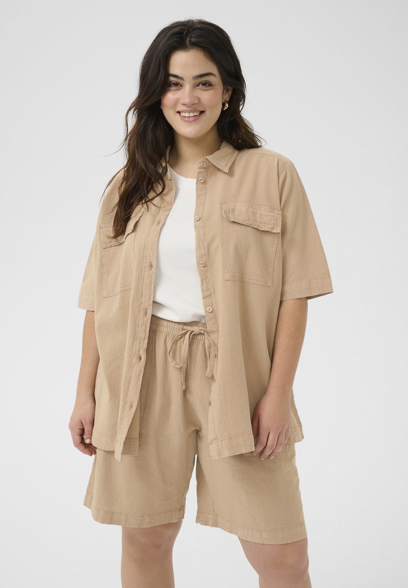 Chemise beige à manches courtes avec un bouton et une poche sur la poitrine, assortie à un short à cordon de serrage. Tissu doux, coupe décontractée, design minimal.