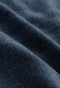 Primo piano di tessuto denim blu scuro che mostra una tessitura strutturata e pieghe diagonali.