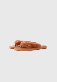 Rjave flip-flop sandale s krznom oblogo in gumijastim podplatom ter teksturirano podnožje. Imajo oznako na traku in minimalističen dizajn.