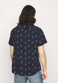 Camisa de manga corta en azul marino con un patrón repetido de pimientos picantes. Confeccionada en tela ligera, presenta un ajuste relajado y cuello clásico.