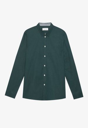 Camisa de manga larga verde oscuro hecha de tela suave, que presenta un collar clásico, cierre delantero con botones y sutiles detalles de costura blanca.