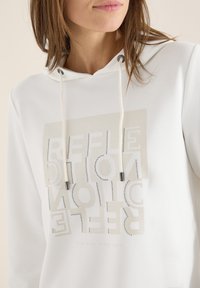 Sudadera blanca con una textura suave, que presenta un gráfico impreso en tonos beige y acentos plateados, capucha con cordón y un diseño de letras moderno.