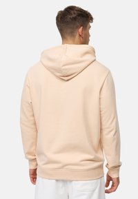 Sudadera de color melocotón claro con una capucha amplia, puños acanalados y dobladillo. Tejido suave con una textura lisa, que presenta un diseño minimalista y sin logotipos visibles.