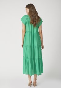 Rochie maxi verde cu mâneci scurte, având un design cu volane și talie strânsă. Materialul moale și ușor se scurge până la glezne.