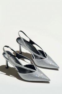 Zilveren slingback hakken met een spitse neus, versierd met rhinestones. Beschikt over een lage stiletto hak en een crisscross bandontwerp.