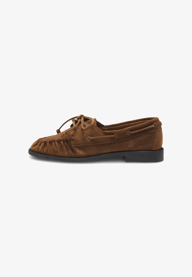 Chaussure style mocassin en daim marron avec une semelle noire, lacets à l’avant et coutures décoratives, vue de profil.