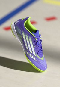 Scarpa sportiva viola con accenti verdi. Presenta una tomaia texturizzata con strisce bianche, un collo imbottito e una suola bianca. Branding audace "F50".