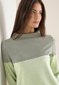 Gestreifter Pullover mit hohem Kragen, oben schwarz-weiße Streifen und unten in hellem Grün, mit glatter, gerippter Struktur.