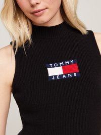 Top senza maniche nero a costine con un'applicazione colorata del logo che presenta "TOMMY" in bianco e "JEANS" in blu su un rettangolo rosso, bianco e blu.