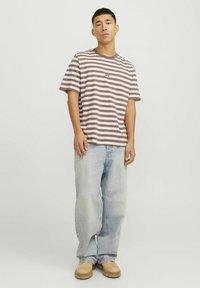 Barna és krém csíkos pamut póló, ribbelős kerek nyakkal, világoskék, laza szabású farmernadrággal és barna slip-on cipővel párosítva.