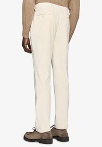 Pantaloni in corduroy bianchi con una vestibilità dritta, caratterizzati da una superficie testurizzata, tasche posteriori, indossati con scarpe in suede marroni.