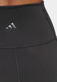 Sorte atletiske legginger med høy midje, glatt tekstur og et reflekterende svart Adidas-logo foran.