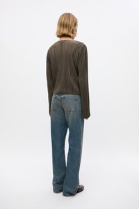 Olijfgroen plissé top met lange mouwen, gecombineerd met lichtblauwe jeans met hoge taille. Gladde textuur, ontspannen pasvorm en recht gesneden ontwerp.