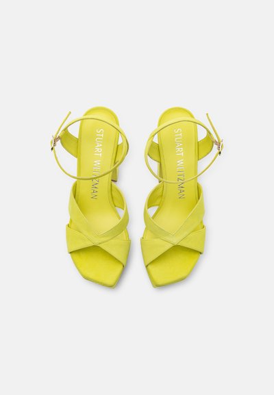 Sandales à talons en daim jaune avec un bout carré, des brides croisées et une sangle de cheville ajustable. Talon légèrement surélevé pour plus de hauteur.