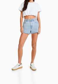 Ljusblå denimshorts med hög midja och uppvikta sömmar, i kombination med en kortärmad vit t-shirt och vita sneakers med gummisula.