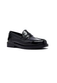 Mocasín de cuero negro brillante con tacón bajo, punta redondeada y detalle decorativo de tachuelas en el borde del tacón, presentado sobre un fondo blanco.