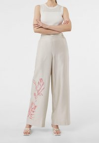 Wijde, lichtbeige broek gemaakt van ademende stof, met een rood botanisch dessin op het linkerbeen en een elastische tailleband.