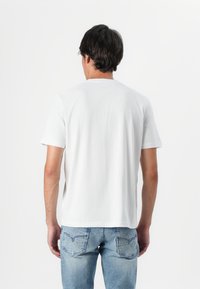 Tricou alb din bumbac cu guler rotund și mâneci scurte. Dispune de o textură netedă și o croială lejeră, combinat cu blugi de culoare albastru deschis.