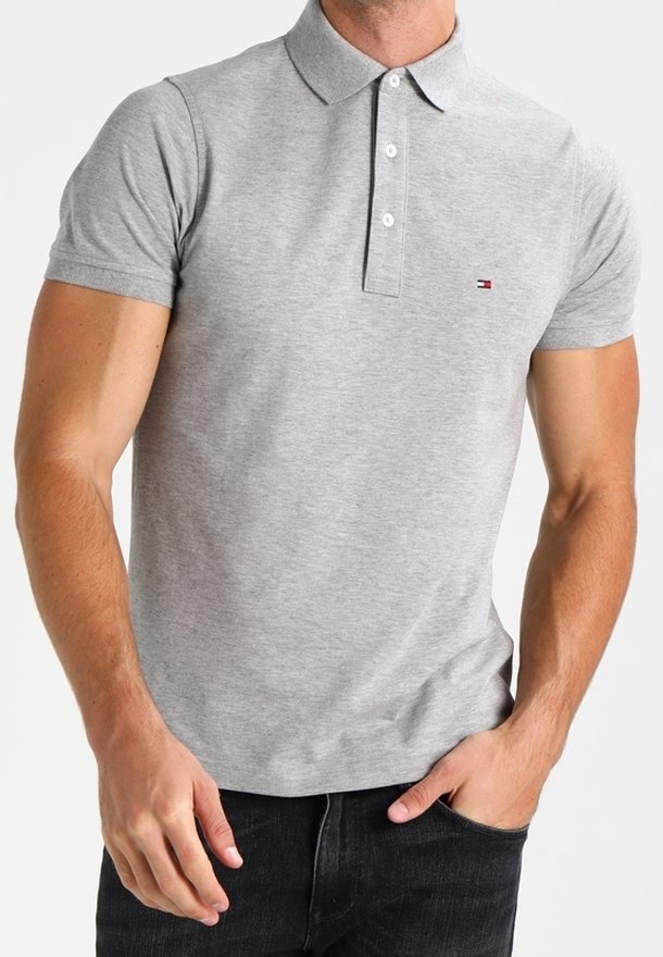 Homme portant un polo ajusté gris clair manches courtes avec trois boutons blancs et un petit logo sur la poitrine gauche, associé à un jean foncé.