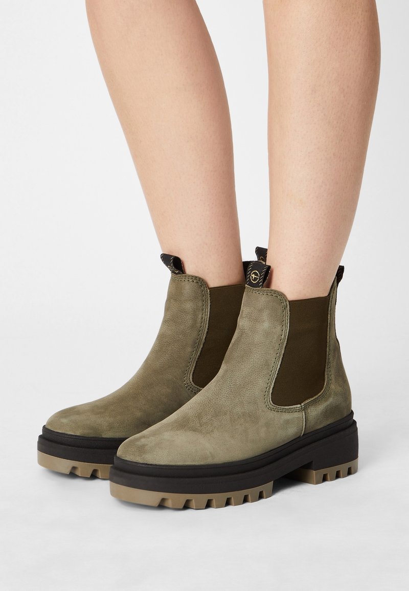 Botas de tobillo de ante verde oliva con paneles laterales elásticos, suela gruesa de relieve y bucles para facilitar su puesta. Textura suave, diseño minimalista.