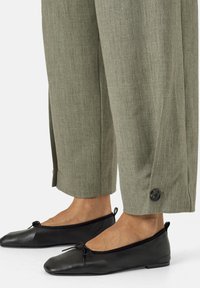 Pantaloni a gamba larga color verde oliva, sartoriali, con una finitura testurizzata e dettagli con bottoni laterali, abbinati a ballerine in pelle nera.