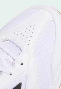 Chaussure de sport blanche avec une combinaison de cuir lisse et de maille texturée. Des accents perforés améliorent la respirabilité. Lacets à l'avant.