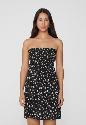 Robe noire sans bretelles avec un motif floral, corsage élastique et jupe ample. Tissu léger avec de petites touches de rose et de vert.