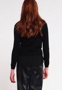 Top nero a maniche lunghe con una textura morbida, caratterizzato da un orlo trasparente a strati, abbinato a una gonna nera in pelle a vita alta.