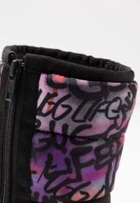 Mustat vetoketjulliset nilkkurit, joissa on violetti- ja vaaleanpunainen graffiti-tyylinen printti. Ominaisuuksia ovat pehmeä tekstiilivarsi ja teksturoitu musta yksityiskohta.
