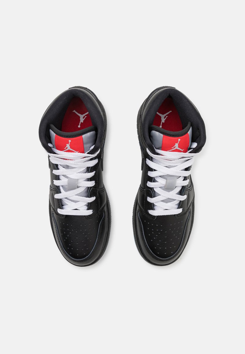 Baskets de basket-ball en cuir noir avec des lacets blancs, des accents rouges et gris, et un cuir perforé pour la respirabilité. Logo iconique sur la languette.