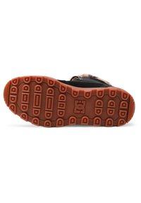 Calzado negro con suela de goma texturizada en naranja. Presenta un dibujo en la banda de rodadura y un logotipo. Ribete de piel de pelo visible en el borde superior.