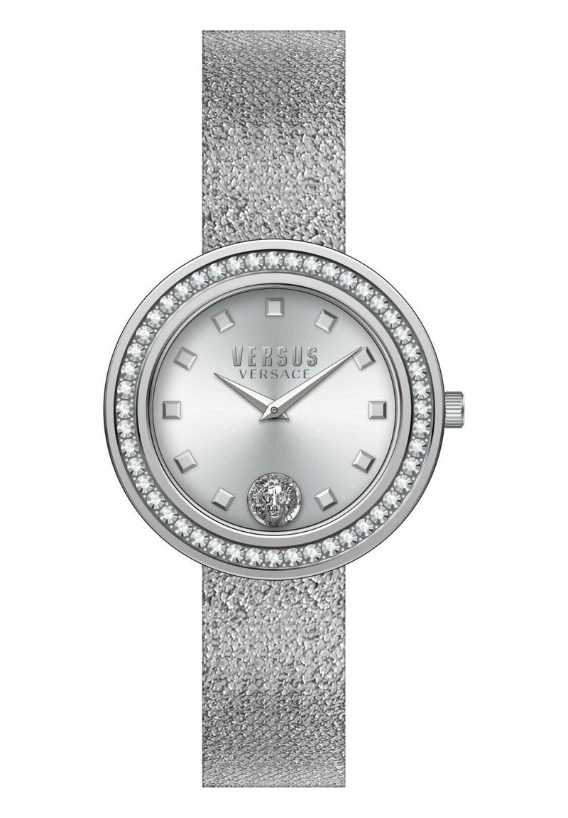 Silberne Analog-Uhr mit einem strukturierten Band, rundem Gehäuse, Kristallakzenten und einem gemusterten Ziffernblatt mit quadratischen Markierungen und einem Logo an der Unterseite.