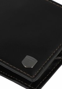 Portefeuille en cuir noir avec des coutures marron et un logo en métal argenté texturé. Présente un design élégant et une forme compacte.