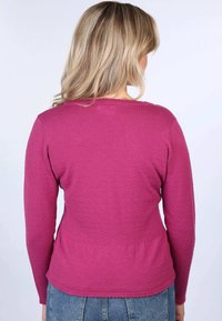 Fitted, long-sleeve top in textured pink fabric with a straight hem. The neckline is rounded, and the back features a subtle scalloped edge.