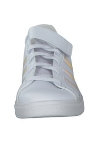 Witte sportieve schoen van glad synthetisch materiaal, met een klittenbandsluiting, veters en drie verticale strepen in glanzend goud aan de zijkant.
