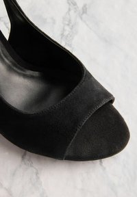 Zwarte nubuck open-teen schoen met een glad leren voering, gebogen randen, gestikte details en een zachte textuur, geplaatst tegen een marmeren achtergrond.