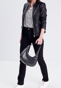 Veste en cuir noire avec un col rond, un chemisier blanc à motifs, un jean noir et un sac à main noir texturé. Des baskets blanches complètent la tenue.