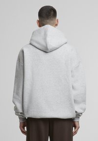Hellgrauer Kapuzenpullover mit großer Kapuze, oversized Schnitt und fallenden Schulternähten. Gefertigt aus weichem Stoff mit gerippten Bündchen und Saum.