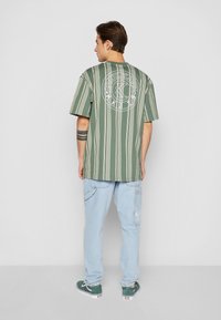 Grönrandig kortärmad skjorta med vit grafik på baksidan, tillsammans med ljusblå jeans och gröna sneakers. Enkel design, avslappnad passform.