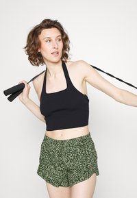 Top cropped preto com textura canelada e decote quadrado, com alças halter, combinado com calções verdes com um padrão de impressão animal em verde escuro.