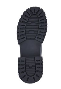 Suela de goma negra con surcos profundos y patrones en zigzag. Presenta ranuras para tracción y una zona central suave. Diseño duradero y resistente.