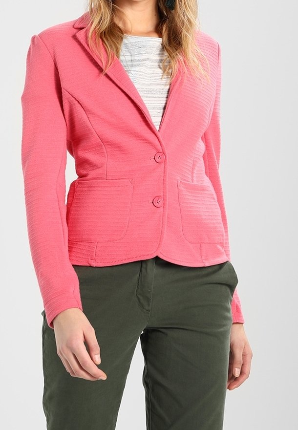 Blazer rose en tissu texturé, avec deux poches avant et une fermeture à deux boutons. Associé à un pantalon vert foncé, au design léger.
