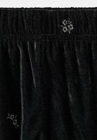 Čierny zamatový materiál s elastickým pásom a malými vyšitými bielymi kvetinovými detailmi blízko hornej a dolnej ľavej strany.