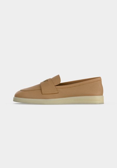Tan leather slip-on loafer with textured upper, flat cream sole, and decorative gold detail on the strap.