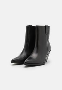 Bottines noires en cuir avec un toe pointu et un talon compensé. Texture lisse avec un design minimaliste et un petit onglet à l'arrière.